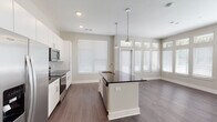 Located in Jacksonville, FL, this single-floor residence offers a thoughtfully designed open-concept layout with a clean, contemporary aesthetic throughout. Dark hardwood-style flooring runs continuously across the living, kitchen, and bedroom areas, providing a cohesive and polished look.

The kitchen is a standout feature, anchored by a large central island with a dark granite countertop, undermount sink, and pendant lighting above. White shaker-style cabinetry extends to the ceiling, complemented by a subway tile backsplash and a full suite of stainless steel appliances including a refrigerator, range, and built-in microwave. Large windows flood the kitchen and adjacent living area with natural light.

The open living area offers generous space and connects seamlessly to the kitchen, creating an ideal layout for daily living. The primary bedroom features soaring ceilings with a ceiling fan and direct access to both a walk-in closet and an en-suite bathroom. The primary bath includes a dual-sink granite vanity with wood-framed mirrors and a glass-enclosed walk-in shower. A second bathroom provides a single granite vanity and additional convenience. A dedicated laundry closet houses a full-size washer and dryer. The hallway provides access to additional closet storage, completing this well-appointed home.