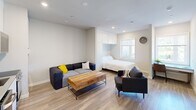Located at 4125 Chestnut St in Philadelphia's University City neighborhood, this thoughtfully designed studio offers a bright, open-concept layout that maximizes every square foot across its single floor. Light wood-tone flooring runs throughout, complementing the neutral white walls and recessed lighting that keep the space feeling airy and well-lit.

The kitchen is fully equipped with stainless steel appliances, including a full-size refrigerator, dishwasher, oven/range, and built-in microwave, all framed by sleek white cabinetry and a clean tile backsplash. An in-unit washer is conveniently integrated into the kitchen area, adding practical functionality. The living area accommodates comfortable seating and a wood-topped coffee table, creating a welcoming lounge space.

The sleeping area features a built-in Murphy bed neatly tucked beneath overhead cabinetry, offering a smart space-saving solution without sacrificing comfort. A window allows natural light to filter into this portion of the unit. The bathroom is finished with gray tile flooring, a single-sink vanity with a gray countertop, and a full tub-shower combination with white subway tile surround and brushed nickel fixtures. Clean lines and a neutral palette define the overall aesthetic of this well-appointed studio.