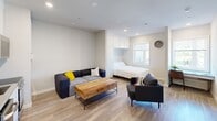 Located at 4125 Chestnut St in Philadelphia's University City neighborhood, this thoughtfully designed studio offers a bright, open-concept layout that maximizes every square foot across its single floor. Light wood-tone flooring runs throughout, complementing the neutral white walls and recessed lighting that keep the space feeling airy and well-lit.

The kitchen is fully equipped with stainless steel appliances, including a full-size refrigerator, dishwasher, oven/range, and built-in microwave, all framed by sleek white cabinetry and a clean tile backsplash. An in-unit washer is conveniently integrated into the kitchen area, adding practical functionality. The living area accommodates comfortable seating and a wood-topped coffee table, creating a welcoming lounge space.

The sleeping area features a built-in Murphy bed neatly tucked beneath overhead cabinetry, offering a smart space-saving solution without sacrificing comfort. A window allows natural light to filter into this portion of the unit. The bathroom is finished with gray tile flooring, a single-sink vanity with a gray countertop, and a full tub-shower combination with white subway tile surround and brushed nickel fixtures. Clean lines and a neutral palette define the overall aesthetic of this well-appointed studio.