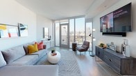 Located at 330 13th St in the heart of San Diego, this contemporary high-rise residence offers a thoughtfully designed single-floor layout that balances modern aesthetics with everyday functionality. The open-concept living area is anchored by expansive floor-to-ceiling windows and a glass-panel balcony door, flooding the space with natural light while framing impressive panoramic views of the San Diego skyline. Light wood-look flooring and a clean, neutral palette give the living room a bright and airy feel, complemented by recessed lighting and a dedicated media wall. The kitchen is well-appointed with light wood cabinetry, a subway tile backsplash, quartz countertops, stainless steel appliances including a gas range, built-in microwave, and dishwasher, along with a peninsula island ideal for casual dining. The bedroom is a tranquil retreat, highlighted by a striking watercolor-inspired feature wall in warm gold tones, plush carpeting, and direct access to the en-suite bathroom. The bathroom features a glass-enclosed walk-in shower with white tile surround, built-in niche shelving, and a clean, minimalist vanity. Throughout the unit, the design emphasizes contemporary finishes, ample storage, and a cohesive modern sensibility suited for urban living.