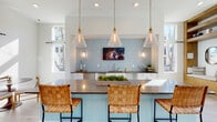 Located at 1100 Hampton Rivers Rd in Charleston, SC, this single-floor clubhouse is designed with a coastal-contemporary aesthetic that blends comfort and sophistication. Light-toned hardwood floors run throughout the open, airy layout, complementing the soaring vaulted ceilings and abundant natural light pouring in through oversized windows and transom glass above.

The main gathering area features a striking stone fireplace wall with a mounted flat-screen TV, surrounded by rattan and upholstered seating — ideal for relaxed socializing. An artful driftwood-style room divider provides a soft visual separation between the lounge and the billiards area, where a full-size pool table anchors the space.

The wet bar area is a standout feature, showcasing soft blue subway tile backsplash, dark countertops, white cabinetry, stainless steel appliances, and pendant lights with glass cone shades suspended on rope. A large island with a light blue base offers bar seating with woven leather stools.

A built-in nook with warm wood shelving and cushioned bench seating adds a cozy reading or conversation corner. Multiple dining tables with mid-century modern chairs are positioned near floor-to-ceiling windows overlooking the surrounding tree line and outdoor pool area, creating a seamless indoor-outdoor connection throughout.