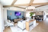 Located at 800 Crawford Street in Portsmouth, Virginia, this thoughtfully designed single-floor space delivers a refined blend of modern style and comfortable living. The open-concept layout is anchored by a striking living area showcasing vaulted ceilings with exposed wood beams and a white shiplap ceiling, creating an airy, architectural focal point. An elegant drum chandelier with pendant accents illuminates the space, while oversized windows flood the room with natural light and frame sweeping views of the surrounding cityscape.

The living area features a warm, neutral color palette complemented by a soft teal accent wall where a large flat-screen television is mounted above built-in cabinetry and shelving, offering both function and visual interest. Rich hardwood flooring flows throughout, tying the spaces together seamlessly.

The gourmet kitchen is outfitted with light-toned cabinetry, dark granite countertops, a striking mosaic tile backsplash, and stainless steel appliances. A central island with bar seating and industrial-style pendant lighting makes it ideal for both cooking and casual dining.

The dining area is enclosed by floor-to-ceiling windows on multiple sides, bathing the space in abundant sunlight and providing expansive urban views. A deep teal ceiling adds a bold, sophisticated contrast to the brightness of the room, creating a dynamic and memorable dining experience.