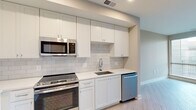 Located at 8787 Georgia Ave in Silver Spring, Maryland, this thoughtfully designed one-bedroom, one-bathroom residence offers a clean, modern aesthetic throughout its efficiently organized single floor. Light wood-tone flooring flows seamlessly across the living room, bedroom, hallway, and kitchen, creating a cohesive and airy feel.

The kitchen is a standout feature, outfitted with white shaker-style cabinetry extending to the ceiling for ample storage, white quartz countertops, a classic subway tile backsplash, and a full suite of stainless steel appliances including a French door refrigerator, range, microwave, and dishwasher. The entry hallway connects directly to the kitchen, providing a practical and welcoming arrival experience.

The living room benefits from large windows fitted with horizontal blinds, allowing generous natural light to fill the space, with views of the surrounding exterior. The bedroom is a comfortable, well-proportioned room with its own large window and includes access to a dedicated closet.

The bathroom is finished with marble-look tile flooring, a wood-toned vanity with a white quartz countertop, an undermount sink, and a glass-enclosed walk-in shower with white subway tile surround. Neutral warm-gray wall tones throughout the residence contribute to a calm, contemporary ambiance.