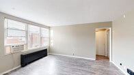 Located at 4817 N Knoxville Ave #2C in Peoria, Illinois, this one-bedroom, one-bathroom unit offers a practical and well-organized single-floor layout. The living room is a bright, open space featuring light gray hardwood-style flooring, neutral beige walls, and large windows that allow generous natural light to fill the room. A wall-mounted heating and cooling unit ensures year-round comfort, while the entry door opens directly into this welcoming area.

The kitchen is efficiently designed with warm oak cabinetry offering ample storage above and below the countertops. Light-toned counters, a double-basin sink positioned beneath a window overlooking greenery, and a white gas range complete the functional cooking space. The hardwood-style flooring continues seamlessly from the living area into the kitchen.

The bedroom is a comfortable, carpeted retreat featuring a ceiling fan with light fixture and a window that brings in natural light and outdoor views. The room offers a well-proportioned footprint suitable for standard bedroom furnishings.

The bathroom includes a shower-over-tub combination with white tile surround, a window with blinds for ventilation and privacy, and a vanity with a warm wood-toned cabinet and mirror. A connecting hallway ties all rooms together, providing a logical and easy-to-navigate flow throughout the unit.