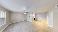 Located in Seabrook, Texas, this single-floor residence offers two bedrooms and two bathrooms within a well-organized, efficient floor plan. The open-concept living, dining, and kitchen area forms the heart of the home, finished with light wood-style flooring and neutral walls that create a bright, clean atmosphere. A ceiling fan with integrated lighting anchors the living space, while a track lighting fixture illuminates the dining area. The kitchen is accessible via a peninsula counter and is equipped with white cabinetry featuring brushed nickel hardware, stone-look countertops, black appliances including a range, microwave, and refrigerator, and ample storage on both sides of the galley-style layout. The primary bedroom is generously sized, featuring plush carpet, a ceiling fan, and access to a private patio through vertical blinds, along with a window that draws in natural light. The second bedroom also features light wood-style flooring, a ceiling fan, and a large window with outdoor views. Each bathroom includes a vanity with stone-look countertops, white cabinetry, brushed nickel fixtures, and a well-lit mirror. Both bedrooms are served by dedicated closets, and a hallway connects the private quarters to the main living areas. The overall ambiance is clean, neutral, and move-in ready.