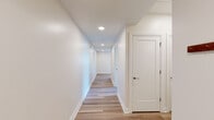 This well-designed single-floor unit presents a clean, contemporary aesthetic throughout. Light wood-style flooring runs consistently across the main living areas and bedrooms, lending warmth and visual continuity to the space. A long, well-lit hallway connects the various rooms, featuring recessed lighting and crisp white walls that create a bright, welcoming corridor.

The unit includes multiple bedrooms, each finished with the same light wood flooring, neutral white walls, and modern black-framed windows that frame views of the surrounding urban and hillside scenery. One bedroom benefits from dual windows, allowing for generous natural light.

The kitchen is outfitted with rich, dark wood cabinetry, granite countertops, and a full suite of stainless steel appliances, including a range, over-the-range microwave, and additional built-in storage.

Two bathrooms serve the unit. One features light stone-look tile flooring, a dark wood vanity, and accessibility grab bars. The second bathroom includes a glass-enclosed walk-in shower with white subway tile surround, matching tile flooring, a window, and a coordinating vanity. A stacked washer and dryer unit is conveniently housed within the hallway, adding practical in-unit laundry access.