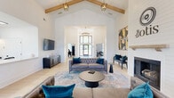 Located at 6001 Thomaston Rd in Macon, Georgia, this single-floor space combines modern farmhouse design with refined, contemporary finishes. The layout encompasses a spacious living room and a well-appointed kitchen, offering a cohesive and functional environment throughout.

The living room immediately impresses with its soaring vaulted ceiling adorned with exposed natural wood beams, creating a striking architectural focal point. Crisp white shiplap walls enhance the bright, airy atmosphere, while large multi-pane windows dressed in sheer white curtains fill the room with abundant natural light and views of the surrounding greenery. A wood-mantel fireplace set into the shiplap accent wall anchors one side of the room, complemented by geometric pendant light fixtures that add a touch of industrial elegance. Light-toned hardwood flooring flows seamlessly throughout the space, reinforcing its clean, open feel.

The kitchen is equally well-designed, featuring white cabinetry, a white quartz countertop island, and a bold teal zellige tile backsplash that serves as a vibrant focal point. Open wood shelving, a stainless steel sink, an under-counter beverage refrigerator, and modern swing-arm sconce lighting complete this functional and visually dynamic space. Together, both rooms create a cohesive, inviting environment well-suited for gathering and entertaining.