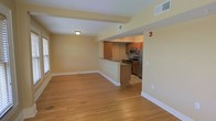 Located at 615 James St in Syracuse, New York, this single-floor residence offers a clean, functional layout designed for comfortable everyday living. The open living area is finished with warm hardwood flooring that extends throughout, complemented by soft yellow-toned walls and crisp white trim that create a welcoming atmosphere. Natural light filters in through windows along the living space, brightening the interior. A peninsula counter connects the living area to the kitchen, providing a natural division between the two spaces while maintaining an open, connected feel. The kitchen is outfitted with warm wood cabinetry, stainless steel appliances including a refrigerator, range, and microwave, and offers ample counter space for meal preparation. Ceiling-mounted lighting and HVAC vents are integrated throughout, ensuring year-round comfort. The overall design is straightforward and practical, with a neutral color palette that provides a versatile backdrop for a variety of interior styles. The single-floor layout ensures easy accessibility and seamless flow throughout the home.