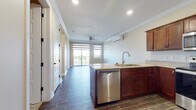 This single-floor residence offers a thoughtfully designed open-concept layout that seamlessly connects the kitchen and living areas. The kitchen is a standout feature, showcasing rich mahogany-toned cabinetry, granite-style countertops, and a full suite of stainless steel appliances including a range, over-the-range microwave, dishwasher, and refrigerator. A peninsula with an undermount sink provides additional prep space and serves as a natural divider between the kitchen and the living area. Wood-look tile flooring runs throughout the main living spaces, adding warmth and durability, while crown molding along the ceilings lends an elevated, polished finish. The living area is bright and airy, benefiting from a sliding glass door that opens to a private balcony, a ceiling fan, and a wall-mounted mini-split HVAC unit for year-round comfort. The bedrooms are carpeted and bathed in natural light through dual-pane windows with modern roller shades, offering a calm and comfortable retreat. The bathroom features a soaking tub with a speckled stone-surround enclosure and classic white fixtures. A hallway with multiple doors provides practical access to the various rooms, completing this well-appointed and functional living space.