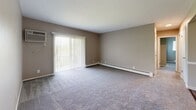 Located at 32 Alan Ct in Florence, Kentucky, this single-floor unit offers a straightforward and functional layout across several well-defined rooms. The living area is generously proportioned, featuring wall-to-wall carpeting in neutral tones, a baseboard heating system, and a large sliding glass door fitted with vertical blinds that allows abundant natural light to fill the space while providing access to an outdoor area. The bedrooms continue the carpeted aesthetic with warm, neutral-toned walls and windows dressed with horizontal blinds that frame views of surrounding greenery. Each bedroom also includes baseboard heating, ensuring consistent comfort throughout. The bathroom is a notable feature, finished with wood-look luxury vinyl plank flooring that adds a touch of warmth. It includes a white vanity with cabinet storage, a mirrored medicine cabinet, overhead lighting, and a full toilet and towel fixtures. The neutral taupe wall color used consistently throughout the unit creates a cohesive and calming ambiance. The floor plan, as seen in the dollhouse view, reveals a compact yet efficient arrangement that includes a kitchen area, living space, bedrooms, and bathroom — all accessible from a central corridor. Overall, the unit presents a clean, move-in ready environment suited for comfortable everyday living.