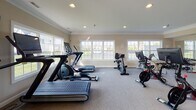 Located at 4623 Lakeside Dr in Maumee, Ohio, this fitness center offers a well-equipped, single-floor exercise facility designed to support a comprehensive workout routine. The space is finished with neutral warm-toned walls, crown molding, and carpeted flooring, giving it a clean and polished appearance.

Natural light streams in through multiple large double-hung windows positioned along the perimeter walls, providing pleasant outdoor views of the surrounding neighborhood and creating an open, inviting atmosphere. Recessed ceiling lighting supplements natural light throughout the space.

The cardio area is well-stocked with treadmills, elliptical trainers, stationary bikes, and a stair climber, catering to a wide range of cardiovascular preferences. A wall-mounted flat-screen television is conveniently positioned for entertainment during workouts. The strength training area features a multi-station cable machine, a workout bench, stability balls, and a full rack of dumbbells spanning various weight increments. A large wall mirror spans one side of the room, enhancing the sense of space and allowing users to monitor their form.

French doors with glass panes provide access to the exterior, further connecting the interior to the outdoors. The overall layout is thoughtfully organized to maximize usability, making this fitness center a functional and welcoming amenity.