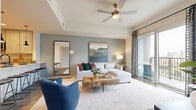 Located in the heart of Charlotte, NC, this single-floor residence offers a thoughtfully designed open-concept layout with modern finishes and urban sophistication. The living room serves as the focal point of the home, featuring a tray ceiling with a ceiling fan, warm wood-look flooring, a sliding glass door leading to a private balcony, and abundant natural light. The space flows seamlessly into a dining area and a well-appointed kitchen outfitted with stainless steel appliances, flat-panel cabinetry, a subway tile backsplash, and generous counter space. A dedicated media area with wood-look flooring and gold-accented cabinetry adds a stylish, functional touch. The bedroom is a standout, boasting floor-to-ceiling windows that frame sweeping views of the Charlotte skyline, a soft carpet finish, and a tray ceiling with a sage green accent wall. The en-suite bathroom features large-format tile flooring, an extended vanity with ample drawer storage, a soaking tub with shower, and a wide mirror with bright overhead lighting. A spacious walk-in closet with built-in shelving and hanging rods completes the private quarters, offering practical storage in a well-sized layout.