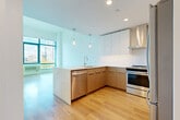 Located at 800 Harbor Blvd in Weehawken, NJ, this well-appointed one-bedroom, one-bathroom residence offers a thoughtfully designed layout with modern finishes throughout. Light wood flooring flows seamlessly across the entire space, complementing the clean, contemporary aesthetic.

The open-concept kitchen is a standout feature, showcasing a large waterfall-edge island with an integrated sink, stainless steel appliances including a refrigerator, range, and dishwasher, and a combination of warm wood and sleek white cabinetry. A stainless steel range hood and stylish pendant lighting complete the look. The kitchen opens directly into the combined dining and living area, creating an airy, connected space ideal for both everyday living and entertaining.

The bedroom is generously sized, featuring tall ceilings, large floor-to-ceiling windows with bold blue frames, and abundant natural light. The urban skyline views add a striking backdrop to the room. Three closets provide ample storage throughout the residence.

The bathroom is finished in a minimalist style with large-format tile flooring, a floating vanity with a vessel sink, a wide mirrored medicine cabinet, and recessed lighting. Additional conveniences include an in-unit laundry area and a dedicated entrance. This residence combines modern design with functional living in a prime Weehawken location.