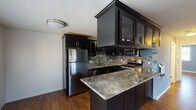 This single-floor space is designed with a cohesive aesthetic that blends modern finishes with functional living areas. Rich hardwood flooring flows seamlessly throughout, tying each room together with warmth and continuity.

The kitchen serves as a standout feature, showcasing dark espresso-toned cabinetry with glass-panel upper doors and sleek hardware. A striking granite peninsula with natural stone veining provides generous prep and serving space, while a full suite of stainless steel appliances—including a refrigerator, gas range, and built-in microwave—adds a polished, contemporary touch. A mosaic tile backsplash in earthy tones accents the cooking area, and a flush-mount ceiling light keeps the space bright and inviting.

The open living area adjoins the kitchen, benefiting from natural light through window-blind-covered windows and a ceiling fan overhead. The layout flows efficiently, with the front entry door visible from the main living space.

The bedrooms feature cool blue-gray painted walls, ceiling fans, and windows with plantation-style blinds that invite natural light. One bedroom includes mirrored sliding closet doors that expand the sense of space visually.

The bathroom is finished with large-format stone-look tile surrounding a soaking tub and shower combination, enclosed by sliding glass doors, offering a clean and refined aesthetic throughout.