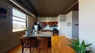 Located at 206 Cherry St SW in downtown Grand Rapids, Michigan, this urban loft-style unit blends industrial character with modern finishes throughout its single-floor layout. Exposed brick walls, dark painted ceilings with visible ductwork, and track lighting establish a distinct loft aesthetic that carries throughout the space.

The open-concept kitchen is a standout feature, showcasing rich dark wood cabinetry, granite countertops, and a full suite of stainless steel appliances including a refrigerator, electric range, microwave, and dishwasher. A granite-topped kitchen island with bar seating provides additional workspace and a casual dining option. Warm hardwood floors extend through the main living and kitchen areas, complementing the industrial aesthetic.

The living area offers a welcoming, cozy atmosphere with a large window framing city views and allowing natural light to filter in against the exposed brick backdrop. The bedroom continues the hardwood flooring and features a warm-toned wood accent column, adding architectural interest to the space.

The bathroom is well-appointed with tile flooring, dark wood cabinetry, a granite vanity countertop, and a large mirror above the sink. Throughout the unit, the thoughtful combination of industrial elements and quality finishes creates a distinctive urban living experience in the heart of Grand Rapids.