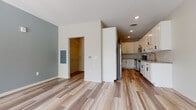 This single-floor space is designed with a clean, contemporary aesthetic carried consistently throughout. Wood-look plank flooring runs continuously across the main living area, kitchen, and bathroom, lending a cohesive, warm feel to the interior. The open living area is bright and airy, highlighted by a large sliding glass door that admits generous natural light and offers views of outdoor greenery. Neutral wall tones, including a subtle blue-gray accent wall, complement the light flooring throughout.

The kitchen is well-appointed with white shaker-style cabinetry featuring black hardware, granite countertops, a classic white subway tile backsplash, and a full suite of stainless steel appliances including a refrigerator, range, microwave, and dishwasher. Recessed lighting illuminates the workspace efficiently.

Adjacent to the living area, a walk-in closet provides organized shelving and hanging space. The bathroom maintains the same refined palette, featuring white cabinetry with black hardware, granite countertops, an undermount sink, a large mirror, and a sliding barn-style door. A stacked washer and dryer unit is also included within the layout, adding practical convenience.