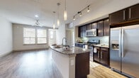 This thoughtfully designed one-bedroom, one-bathroom unit offers an efficient and modern layout across a single floor. The open-concept kitchen and living area serves as the heart of the space, where wood-style plank flooring flows seamlessly throughout. The kitchen is equipped with dark espresso cabinetry, granite countertops, a subway tile backsplash, stainless steel appliances, and track lighting overhead. A peninsula island with pendant lighting above provides additional counter space and casual seating, while overlooking the living area, which features a ceiling fan and natural light from multiple windows with views to the exterior.

A hallway connects the main living area to the private bedroom, bathroom, and closet. The bedroom is carpeted and benefits from two windows that bring in natural light. The walk-in closet features wire shelving on three walls, offering generous storage capacity. The bathroom presents dark cabinetry with granite countertops, a large mirror with vanity lighting, wood-style tile flooring, and a full tub-shower combination with tiled surround. The overall palette is neutral and contemporary throughout.