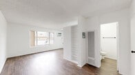 Located at 238 S Serrano Ave in the vibrant Koreatown neighborhood of Los Angeles, this single-floor unit offers a clean, modern aesthetic defined by crisp white walls, textured ceilings, and light-toned wood-style flooring that runs consistently throughout the space.

The open-plan living and kitchen area forms the heart of the unit. A large sliding window allows natural light to fill the living space, creating a bright and airy atmosphere. The kitchen is efficiently designed with white cabinetry featuring matte black hardware, granite-style countertops, a stainless steel sink with a modern pull-down faucet, a gas range, and a full-size refrigerator. A peninsula counter provides a natural division between the kitchen and living area, along with open shelving for additional storage.

A wall-mounted heating and cooling unit in the main hallway ensures year-round climate control. The bedroom is a well-proportioned, quiet room with the same consistent flooring and neutral white walls, offering a versatile and functional space.

The bathroom is thoughtfully appointed with a vanity featuring a warm stone-toned countertop, a single undermount sink, matte black fixtures, a large framed mirror, overhead cabinetry, and open shelving. The overall design of the unit emphasizes clean lines, functional layouts, and a neutral palette suited to a variety of personal styles.
