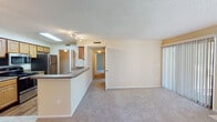 This single-floor residence in Jacksonville, FL (32218) offers a functional and comfortable layout with a warm, neutral aesthetic throughout. The open-concept kitchen is well-equipped with light wood cabinetry, dark granite-style countertops, stainless steel appliances including a refrigerator, range, and microwave, and wood-look flooring. A peninsula breakfast bar seamlessly connects the kitchen to the dining and living areas, making the space ideal for everyday living and entertaining. The spacious living room is a standout feature, highlighted by a tile-surround fireplace, plush carpeting, and a sliding glass door fitted with vertical blinds that opens to an outdoor area, allowing generous natural light to fill the room. A dedicated dining area sits adjacent, complete with a pendant light fixture. The bedrooms are generously sized, each featuring carpet flooring, large windows with outdoor views, and ample closet space. A bathroom with warm wood vanity cabinetry, a well-lit mirror, and a walk-in closet nearby adds convenience and practicality. Textured ceilings are consistent throughout the home, contributing to the classic residential character of this Jacksonville property.