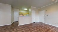 This single-story unit is finished consistently throughout with dark, wood-style vinyl plank flooring and neutral beige walls, creating a cohesive and practical aesthetic across all spaces. Crown molding accents the living area and select rooms, adding a subtle architectural detail to the otherwise straightforward design.

The open living area is well-proportioned, featuring track lighting and direct sightlines to the kitchen, which is separated by a half-wall peninsula. The kitchen is laid out in a galley configuration with light wood cabinetry, white laminate countertops, and white appliances including a refrigerator, dishwasher, and microwave. An electrical panel is accessible via a dedicated utility closet off the kitchen.

The unit includes multiple bedrooms, each with wood-style flooring, window blinds for natural light control, and individual closets. One bedroom features a walk-in closet, while another includes a ceiling fan and crown molding. Two bathrooms serve the unit: one with a tub/shower combination, single vanity, and light wood cabinetry, and a second more compact bathroom with a shower and basic fixtures. Both bathrooms continue the wood-style flooring found throughout the unit.