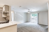 This single-floor residence offers a thoughtfully designed open-concept layout that seamlessly connects the living, dining, and kitchen areas. The spacious living room is finished with plush carpeting, crown molding, and a ceiling fan, while a large sliding glass door allows natural light to flow in and provides access to an outdoor balcony area. The kitchen is well-equipped with stainless steel appliances, including a refrigerator and an electric range, complemented by gray cabinetry, white countertops, and a striking mosaic tile backsplash. A breakfast bar peninsula bridges the kitchen and living area, adding both function and style. Hardwood-style flooring extends through the kitchen and bathrooms, creating a clean contrast to the carpeted living spaces. The bedrooms are generously sized, each featuring plush carpet and ceiling fans. The primary bedroom includes a walk-in closet with built-in shelving, while an additional bedroom offers a mirrored sliding-door closet. The bathrooms are finished with gray vanity cabinetry, white countertops, and a tub-shower combination, with one bathroom also featuring accessibility grab bars. Crown molding and recessed lighting throughout add refined finishing touches to this comfortable and functional home.