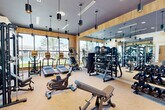 Located at 1505 Cornerstone Blvd in Daytona Beach, FL, this fitness center offers a thoughtfully designed exercise space that balances functionality with modern aesthetics. The single-floor layout provides a generous workout area filled with a comprehensive selection of Matrix-brand cardio equipment, including treadmills, ellipticals, and stationary bikes. The strength training zone is equally well-appointed, featuring a multi-functional cable machine, adjustable benches, a full dumbbell rack, kettlebells, and stability balls.

The room's design is a standout feature, with warm wood-paneled walls and a bold dark ceiling that create a sleek, contemporary atmosphere. Stylish cylindrical pendant lights hang throughout, adding focused illumination. A large floor-to-ceiling window spans one wall, flooding the space with natural light and offering outdoor views of the surrounding community and landscaping. Full-length mirrors on the opposite wall visually expand the room while serving a practical purpose for form-checking during workouts.

Coastal-themed wall murals add a distinctive local touch, tying the space to its Florida setting. The neutral carpeted flooring provides comfort underfoot, and the overall ambiance is both motivating and inviting — making this fitness center a standout amenity.