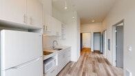 Located at 5460 N Interstate Ave in Portland, Oregon, this modern 2-bedroom, 1-bathroom unit offers a thoughtfully designed layout with contemporary finishes throughout. Light wood-tone flooring runs continuously across the entire space, complementing the clean white walls and creating a bright, cohesive aesthetic.

The kitchen is efficiently designed with white flat-front cabinetry, open shelving, light countertops, a stainless steel sink, and built-in appliances including a refrigerator and microwave. A large window floods the kitchen with natural light and frames views of the surrounding Portland cityscape.

The open hallway connects the kitchen to both bedrooms and the shared bathroom, making for a functional and easy-to-navigate floor plan. The bedrooms are simply designed with neutral walls and light flooring, with windows that invite ample daylight. The primary bedroom features oversized floor-to-ceiling windows offering expansive views of the neighborhood.

The bathroom is finished in a clean, modern style with a white vanity, integrated sink, chrome fixtures, and a large mirror. Notable throughout the unit are the impressively tall ceilings, which enhance the sense of openness and volume despite the compact footprint.