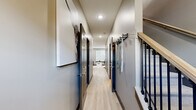 This two-story home in Elizabethtown, Kentucky offers a well-designed layout across two floors, featuring two bedrooms, three bathrooms, and an attached garage. The main level opens into a combined kitchen and living area anchored by a large kitchen island with a white quartz countertop and seating for multiple bar stools. Rich warm-toned cabinetry reaches toward the ceiling, complemented by stainless steel appliances and light wood-look flooring that extends throughout the main living spaces. The living area is comfortable and open, with natural light and modern styling. A half bath on the main floor provides added convenience. A clean, well-lit hallway connects the key areas of the home, featuring recessed lighting and light hardwood flooring, with a staircase leading to the upper level. Upstairs, the primary bedroom is generously sized, offering plush carpeting, a ceiling fan, and natural light from a bright window. The second bedroom mirrors a similar aesthetic with soft tones and comfortable proportions. The bathrooms include a full tub-and-shower combination with clean white finishes. The attached garage features a standard sectional door with an automatic opener and concrete flooring, offering practical everyday storage and parking. The home's neutral color palette and modern finishes create a cohesive, inviting atmosphere throughout.