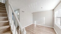 Located at 2002 Cedar Fork Dr in Greensboro, NC, this two-story, 2-bedroom, 2-bathroom home offers a well-organized layout across two floors. The main level features a bright living room with light-toned luxury vinyl plank flooring, neutral warm-gray walls, and a white staircase railing leading to the upper level. Natural light streams in through window treatments, lending a clean, airy feel throughout. The combined dining room and kitchen is a functional highlight, featuring crisp white shaker-style cabinetry, white countertops, a stainless steel dishwasher, range, and refrigerator — all complemented by wood-look flooring and a window for added brightness. Upstairs, both bedrooms are carpeted for comfort and include ceiling fans and ample closet space. The primary bedroom offers a generous footprint with dedicated closet storage, while the secondary bedroom features louvered bifold closet doors. The two bathrooms include wood-look flooring; one features a tub/shower combination with tiled surround and louvered storage closet. With seven closets total, a dedicated laundry area, and two staircases providing convenient access, this home prioritizes practical storage and efficient use of space. Textured ceilings are present throughout.
