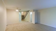 This three-floor home offers a practical and well-organized layout designed to accommodate a variety of living needs. The main living area is finished with wall-to-wall carpeting that adds warmth and comfort underfoot, while neutral-toned walls provide a clean, versatile backdrop throughout. A ceiling fan with an integrated light fixture is centrally positioned, contributing to both airflow and ambient lighting in the space.

A central staircase with a sleek metal railing serves as the visual focal point of the main level, connecting all three floors and creating a sense of vertical continuity. The stairwell is flanked by doorways that lead to additional rooms, suggesting a thoughtfully compartmentalized floor plan. Transom-style windows above the doorways allow natural light to filter through, brightening the interior even in areas away from exterior walls.

Crown molding adds a subtle architectural detail along the ceiling line, lending a polished finish to the space. The overall design maintains a straightforward, functional aesthetic with clean lines and a neutral palette, making it highly adaptable to a range of furnishing styles. With multiple levels to explore, this home provides ample space for both everyday living and flexible use across its various rooms and areas.