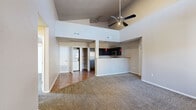 Located at 1335 Pullman Dr in El Paso, TX, this single-story, 3-bedroom, 2-bathroom home offers a well-designed layout with a seamless flow between living spaces. The open-concept living room immediately impresses with dramatically high ceilings and a ceiling fan overhead, creating a bright and airy atmosphere. A large front window invites natural light into the carpeted living area, which transitions to hardwood-style flooring near the entryway. The kitchen is a functional highlight, featuring dark cabinetry, stainless steel appliances including a gas range, microwave, and refrigerator, granite-style countertops, and bold red pendant lighting that adds a touch of character. A raised breakfast bar separates the kitchen from the living space. In-unit laundry is also accessible from the kitchen area. The three bedrooms are carpeted and comfortably sized, each equipped with ceiling fans and windows allowing natural light. The primary bedroom offers a generous closet and elevated architectural detailing. The two bathrooms are finished with tile flooring and granite-style vanity counters; one features a soaking tub with tiled surround, while the other includes a tub-shower combination with a window for ventilation.