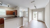 Located at 928 Timber Valley Way in Virginia Beach, Virginia, this single-floor residence offers a well-designed layout with a blend of comfort and functionality. The open-concept kitchen is equipped with rich cherry wood cabinetry, dark granite-style countertops, black appliances including a full-size refrigerator, and a peninsula that provides both additional prep space and a natural transition into the living and dining areas. Track lighting illuminates the kitchen, while crown molding adds a refined touch throughout the common areas. The living area features warm hardwood-style flooring and is bathed in natural light from multiple windows and a glass door that opens onto a private balcony. The balcony offers pleasant views of mature pine trees and the surrounding community. Bedrooms are finished with plush carpeting and ceiling fans, with windows that bring in additional natural light. The bathroom includes a full tub-shower combination with tiled surround, a vanity with under-sink storage, and wood-style flooring. Neutral warm-gray tones are consistent throughout the unit, creating a cohesive and inviting atmosphere. The overall design is clean, practical, and move-in ready.