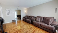 This two-floor townhouse offers a well-organized layout designed for comfortable everyday living. The main level features a spacious living room with warm, honey-toned hardwood flooring that extends throughout much of the home, neutral-toned walls, and natural light streaming in through front-facing windows. The living area flows conveniently into a separate dining space, which features tile flooring and accommodates a raised dining table with seating for four. Adjacent to the dining area, the kitchen is outfitted with ample honey oak cabinetry, dark countertops, tile flooring, and white appliances including a refrigerator, electric range, and built-in microwave. The two bedrooms, both featuring the same warm hardwood floors, offer comfortable proportions with natural light from windows fitted with blinds. One bedroom includes a built-in wardrobe, providing useful storage. The full bathroom is equipped with a shower-tub combination. Throughout the home, the neutral color palette and consistent flooring choices create a cohesive and welcoming atmosphere, making this townhouse a practical and livable space across both its floors.