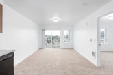 This well-designed single-floor residence offers a clean, contemporary aesthetic with a thoughtful layout that maximizes comfort and functionality. The open-concept living and dining area is generously proportioned, featuring soft wall-to-wall carpeting, crisp white walls, and abundant natural light streaming through large sliding glass doors that lead to a private balcony with views of surrounding greenery and the neighborhood below.

The kitchen is outfitted with warm wood-toned cabinetry, neutral countertops, and a full suite of black appliances including a range, over-the-range microwave, refrigerator, and dishwasher. Open shelving and ample cabinet storage provide practical functionality, while light hardwood-style flooring ties the space together seamlessly.

The bedroom is a comfortable, carpeted retreat with a large window framing pleasant outdoor views, filling the room with natural light and creating a calm, airy atmosphere.

The bathroom maintains the unit's modern sensibility with light hardwood-style flooring, a wood-toned vanity with an integrated sink, recessed lighting, and a clean, minimalist finish.

Throughout the space, a consistent palette of whites, warm wood tones, and neutral textures creates a cohesive and inviting environment. The unit's single-floor design ensures easy navigation and a smooth, connected flow between all living spaces.