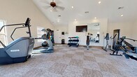 Located at 925 Tiny Town Rd in Clarksville, Tennessee, this well-equipped fitness center offers a bright and spacious environment designed to support a wide range of workout routines. The room features striking vaulted ceilings that create an open, airy atmosphere, complemented by recessed lighting and a ceiling fan that ensures comfortable air circulation during workouts. Neutral-toned carpet tile flooring spans the entire space, providing a clean and practical surface throughout.

Multiple windows positioned along the walls flood the room with natural light, enhancing the overall sense of openness. Two exterior doors provide convenient access from different points. A large wall-mounted mirror and flat-screen television are also present, adding both functionality and entertainment to the workout environment.

The fitness center is outfitted with an impressive array of cardio equipment, including treadmills, an elliptical trainer, a stair climber, and a rowing machine. A multi-station cable machine supports a variety of strength training exercises, while a dedicated free weight area features a tiered dumbbell rack with an assortment of weights and an adjustable bench. Stability balls and additional accessories round out the available equipment, making this fitness center a comprehensive facility for residents seeking a convenient on-site workout space.