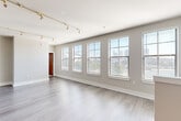 This single-floor unit offers a well-organized layout comprising three bedrooms, two bathrooms, a combined kitchen and living area, and two hallways. The living room is a standout space, characterized by a row of large double-hung windows fitted with horizontal blinds that allow generous natural light to fill the room. Track lighting runs along the ceiling, providing additional illumination, while light wood-style flooring ties the space together with a clean, modern aesthetic.

The kitchen is open to the living area and features warm honey-toned cabinetry, dark countertops, tile flooring, a stainless steel range, a dishwasher, and a double sink—offering a functional layout within a compact footprint.

The bedrooms vary in configuration: the primary bedroom includes light wood-style flooring and windows with outdoor views, while the secondary bedrooms feature plush carpeting and natural wood doors, adding warmth to the neutral palette. One bedroom includes a closet door and direct hallway access.

Both bathrooms are finished with wood-toned vanities and dark hardwood-style flooring. One bathroom includes a tiled tub-shower combination, while the other features a glass-enclosed walk-in shower. Neutral gray walls are consistent throughout the unit, contributing to a cohesive and understated overall ambiance.