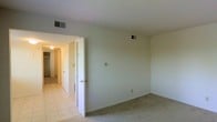 This single-floor residential space offers a straightforward and functional layout designed for comfortable everyday living. The main room features wall-to-wall carpet underfoot, contributing to a warm and quiet atmosphere, while the adjoining hallway transitions to easy-to-maintain tile flooring. The space is finished with smooth, neutral-toned walls and a textured ceiling, giving each room a clean and understated aesthetic.

Multiple interior doors visible from the main room provide access to additional spaces, which appear to include a closet and connecting rooms, suggesting a practical arrangement that supports organization and storage. Ceiling-mounted HVAC vents are present throughout, ensuring climate control across the space. Overhead lighting fixtures illuminate the hallway, adding to the overall brightness of the interior.

The open wall space in the main room offers flexibility in furniture arrangement, allowing the room to be configured to suit a variety of needs. The transition between the carpeted room and the tiled hallway creates a clear distinction between living and utility areas. Overall, this space presents a clean, move-in-ready environment with a neutral palette that serves as a versatile canvas for personalization.