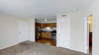 This single-floor unit at Windmill offers a practical and functional layout designed for comfortable everyday living. The living area features neutral-toned carpet that extends throughout, creating a warm and cohesive feel. The space opens directly into the kitchen, providing an open-concept flow ideal for both daily routines and entertaining.

The kitchen is outfitted with stainless steel appliances, including a refrigerator and a gas range, complemented by warm wood-toned cabinetry that lines the walls and provides ample storage. Dark countertops contrast cleanly against the cabinetry, and a sink is positioned beneath overhead cabinets, maximizing workspace efficiency. The kitchen transitions to hard surface flooring, offering a durable and easy-to-maintain area. A louvered door nearby hints at additional storage or utility access.

The unit features a textured ceiling throughout and neutral white walls that keep the space feeling bright and open. Overhead lighting and a ceiling vent indicate central climate control. The overall aesthetic is clean and move-in ready, making it a solid and well-appointed space at the Windmill property.