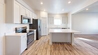 This two-story home offers a clean, modern design with a neutral color palette and thoughtful finishes throughout. The main level features an open living area bathed in natural light from large windows fitted with blinds, complemented by plush wall-to-wall carpeting and a ceiling fan with overhead lighting. An arched entryway connects the living space to the kitchen, which is equipped with white shaker-style cabinetry, light quartz countertops, a double stainless steel sink, stainless steel appliances including a refrigerator and dishwasher, and wood-look tile flooring that adds warmth to the space. A convenient half bath is also located on the main level. The staircase leads to the upper floor, where multiple carpeted bedrooms each feature windows that let in ample natural light and offer views of the surrounding neighborhood. The primary bedroom stands out with soaring vaulted ceilings and direct access to a well-organized walk-in closet outfitted with custom light wood shelving, hanging rods, and built-in drawers. A full bathroom with a tub-shower combination and tile flooring serves the upper level. Throughout, the home maintains a bright, move-in-ready atmosphere with consistent finishes and a practical, functional layout.