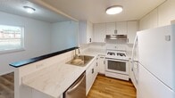Located at 4100 W 19th Ave in Stillwater, Oklahoma, this two-floor home offers a practical and updated living environment with a clean, neutral aesthetic throughout. The kitchen is a standout feature, equipped with white cabinetry accented by black hardware, marble-look quartz countertops, a stainless steel sink, a gas range, dishwasher, and refrigerator — all complemented by warm hardwood-style flooring and a pass-through window that connects to the adjacent living area. The living space showcases the same hardwood-style flooring and is highlighted by a distinctive exposed brick column, adding a touch of architectural character to the otherwise modern interior. Bedrooms are finished with plush carpeting and ceiling fans, providing comfort and climate control. Windows with blinds allow for natural light while maintaining privacy. The bathroom features a tub-shower combination with tile surround, a toilet, wood-look flooring, and a vanity with a quartz-style countertop, white cabinetry, and a round mirror with modern wall-mounted lighting. Textured ceilings are consistent throughout the home, contributing to its classic residential character. The two-floor layout offers practical separation of living and private spaces.