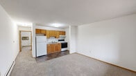 Located in Marion, Iowa, this single-floor unit offers a straightforward and functional layout designed for comfortable everyday living. The open-concept kitchen and living area form the heart of the space, with the kitchen featuring warm honey-toned wood cabinetry, a double-basin stainless steel sink, a white electric range with overhead ventilation, and a full-size refrigerator. Dark stone-patterned tile flooring anchors the kitchen zone, transitioning seamlessly into the carpeted living area, which receives natural light through a window overlooking a neighboring outdoor area and balcony. The unit includes two bedrooms, both finished with neutral wall-to-wall carpeting and natural wood-trimmed doors. Each bedroom features a window with horizontal blinds, allowing for ample daylight, and includes closet storage. One bedroom is equipped with a wall-mounted air conditioning unit and a baseboard heater, providing year-round climate control. Baseboard heating is also present in the living area. The full bathroom is appointed with dark tile flooring matching the kitchen, a single-sink vanity with wood cabinetry, a toilet, and a tub-shower combination with a navy curtain. Throughout the unit, clean white walls and consistent wood trim detailing create a cohesive and practical interior environment.