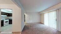 Located at 1600 Laurel Rd in Lindenwold, NJ, this single-floor unit offers a practical and comfortable layout across several well-defined living spaces. The living room is generously sized, featuring neutral-toned wall-to-wall carpeting, clean white walls, and a large sliding glass door dressed with vertical blinds that floods the space with natural light and provides access to outdoor greenery views. An additional window in the secondary carpeted room further enhances the natural light throughout.

The kitchen is equipped with dark-stained cabinetry featuring raised-panel doors, dark granite-style countertops, and white appliances including a gas range, dishwasher, and refrigerator. Light tile flooring runs throughout the kitchen and entry areas, complementing the overall neutral palette. A hallway connects the kitchen to the rest of the unit seamlessly.

The bedroom areas are carpeted and offer ample wall space, with closet access and connecting doors. The bathroom showcases a retro aesthetic with sky-blue wall tiles, a classic black-and-white mosaic tile floor, a white vanity with mirror, and a full tub-shower combination, creating a distinctly vintage yet functional feel throughout.