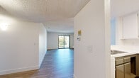 Located in San Diego, CA, this single-floor residence offers 2 bedrooms and 2 bathrooms within a well-organized layout. The combined kitchen and living room serves as the heart of the home, where wood-look laminate flooring extends throughout the open space. The kitchen is equipped with white upper cabinetry, taupe lower cabinetry, white appliances including an electric range and refrigerator, and a tile-topped breakfast bar that provides additional counter and seating space. The living room is bright and airy, featuring a sliding glass door that opens to an outdoor balcony with natural views beyond. Both bedrooms are carpeted and receive natural light through horizontal-slatted windows. The generously sized primary bedroom offers ample room for furnishing. Each bathroom features wood-look flooring, taupe cabinetry with white countertops, a framed mirror with overhead lighting, and a full bathtub with a curved shower rod. Clean white walls and textured ceilings are consistent throughout, contributing to a bright, neutral aesthetic. Two hallways connect the spaces efficiently, rounding out a functional and cohesive floor plan suited for comfortable everyday living.