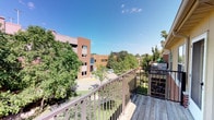 This single-floor space is distinguished by its expansive outdoor deck, which serves as a standout architectural feature. The deck is constructed with wood planking and enclosed by a sturdy metal railing, providing both safety and an open, airy feel. From this elevated vantage point, occupants enjoy panoramic views of a vibrant, tree-lined urban courtyard below, with mature deciduous trees providing generous greenery throughout. The surrounding environment features classic multi-story brick buildings, characteristic of an established urban or campus-style setting, framed by wide-open skies that flood the outdoor area with natural light. The courtyard below includes paved walkways, landscaped areas, and accessible open space, contributing to the active and communal character of the neighborhood. The deck's orientation captures broad sightlines in multiple directions, enhancing the sense of openness. The overall ambiance of the space is defined by this strong indoor-outdoor connection, with the deck acting as a private retreat that overlooks a well-maintained and lively exterior environment. The interior portions of the space were not fully captured in available imagery, but the outdoor deck alone offers a compelling and functional feature central to the character of this property.