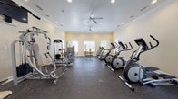 The fitness center at 111 Coopers Ridge Blvd in Ladson, South Carolina is a well-equipped, single-floor facility designed to support a comprehensive workout routine. The space is finished with warm, light yellow walls, crisp crown molding, and durable rubber flooring that provides both comfort and safety underfoot. Recessed lighting throughout, paired with multiple ceiling fans, ensures the room remains well-lit and well-ventilated during any workout.

The facility is generously outfitted with a wide variety of equipment. Cardio options include multiple treadmills, elliptical trainers, and a stationary recumbent bike, while a rowing machine rounds out the aerobic offerings. For strength training, the space features several multi-function cable and resistance machines, as well as a dedicated free-weight area stocked with kettlebells of varying sizes on a standing rack.

Natural light filters in through multiple windows fitted with horizontal blinds, offering views of the surrounding outdoor greenery and lending the space an open, airy feel. A glass door provides direct access to the exterior, further connecting the interior to the outdoors. The overall ambiance is clean, organized, and functional, making this fitness center a practical and inviting amenity for residents of the Coopers Ridge community.