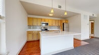 Located at 1373 Mt Hope Ave in Rochester, NY, this 2-bedroom, 2-bathroom residence offers a clean, modern aesthetic with consistent finishes throughout. The open-concept kitchen is a standout feature, showcasing warm honey-toned cabinetry, a mosaic tile backsplash, white quartz countertops, stainless steel appliances, and a large central island with pendant lighting overhead. Rich hardwood-style flooring flows through the kitchen and into the combined dining and living area, which benefits from multiple windows that invite natural light. Both bedrooms are carpeted and well-sized, with the spacious primary bedroom featuring a large window with neighborhood views. The two bathrooms mirror each other in design, each offering a tub/shower combo, a light wood vanity with white countertop, a large mirror, and warm hardwood-style flooring. Three closets provide ample storage throughout. A dedicated laundry area and basement add practical convenience. The entryway features the same hardwood-style flooring along with an accessible electrical panel. Neutral wall tones and consistent finishes throughout give the space a cohesive, move-in-ready feel suited for comfortable everyday living.