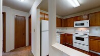 Located at 11751 W River Hills Dr in Burnsville, Minnesota, this single-floor unit offers a practical and comfortable layout. The kitchen is well-appointed with warm oak cabinetry extending to the ceiling, white appliances including a refrigerator, range, dishwasher, and built-in microwave, along with generous counter space and a stainless steel sink. A breakfast bar provides a casual dining option and creates an open connection to the adjacent living areas.

The living room is generously sized, featuring neutral carpet, a ceiling fan, baseboard heating, and a large sliding glass door that opens to a private balcony with outdoor views of the surrounding greenery. The space transitions seamlessly between carpeted and hardwood-style flooring zones.

The bedrooms are comfortably scaled with plush carpet, baseboard heating, and windows that bring in natural light and views of the mature trees outside. One bedroom also includes a wall-mounted air conditioning unit for personalized climate control.

The unit includes two bathrooms: one featuring a full tub-shower combination with white tile surround, and a second with a glass-door shower enclosure. Both bathrooms are finished with tile flooring and clean, neutral tones. Textured ceilings are consistent throughout, contributing to the unit's classic residential character.