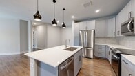 This well-designed 2-bedroom, 2-bathroom residence offers a thoughtful single-floor layout with modern finishes throughout. The open-concept kitchen and living area serves as the heart of the home, anchored by a large center island with a white quartz countertop, double undermount sink, and integrated dishwasher. Gray shaker-style cabinetry reaches toward the ceiling, complemented by a herringbone tile backsplash and a full suite of stainless steel appliances, including a French door refrigerator and range. Sleek pendant lights add a contemporary touch above the island. The living area features warm hardwood-style flooring, a ceiling fan, and French doors that invite natural light and outdoor views. Both bedrooms are comfortably sized, each with natural light from well-placed windows and ceiling fans. The primary bedroom includes a spacious walk-in closet outfitted with built-in shelving and hanging rods for ample storage. A second closet provides additional organization options. The bathrooms are clean and modern, with one featuring a tiled tub-shower surround in a neutral palette with brushed nickel fixtures. Consistent hardwood-style flooring, soft neutral wall tones, and recessed lighting tie the entire space together cohesively.
