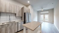 Located at 2717 Minimax Dr in Houston, TX, this well-appointed single-story unit offers a thoughtfully designed layout across a compact yet efficient floor plan. The open-concept kitchen and living area serves as the heart of the home, featuring light wood-grain cabinetry extending to the ceiling, quartz countertops, a white tile backsplash, and a full suite of stainless steel GE appliances including a gas range, built-in microwave, dishwasher, and a French-door refrigerator. The living area is bright and airy, highlighted by a ceiling fan and a set of French doors with transom window that invite abundant natural light and provide outdoor views. Wood-look flooring runs throughout the main living spaces, adding warmth and continuity. The bedroom offers plush carpeting underfoot, a ceiling fan, and ample closet space with multiple doors leading to storage and the adjacent hallway. The bathroom is finished with large-format tile flooring, a wood-tone vanity with quartz countertop, an overhead storage cabinet, and a framed mirror. A dedicated laundry area adds everyday convenience. The neutral color palette and clean finishes throughout create a modern, move-in-ready atmosphere.