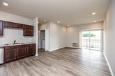 This single-floor residence offers a well-designed layout with a cohesive, modern aesthetic throughout. The kitchen is a standout feature, showcasing rich dark-mahogany cabinetry extending to the upper walls, white countertops, and a full suite of stainless steel appliances including a refrigerator, range, and microwave. Light hardwood-style flooring runs through the main living and kitchen areas, contributing to a clean, contemporary feel. The open living area flows naturally toward sliding glass doors that lead to a private balcony, offering views of an open, scenic landscape.

Two carpeted bedrooms each feature individual wall-mounted HVAC units, windows with outdoor views, and ceiling fans for added comfort. Each room is served by its own bathroom: one includes a full tub-shower combination with light hardwood-style flooring and a dark-cabinet vanity, while the second features a single vanity with a large mirror and a separate shower area.

A dedicated in-unit laundry closet houses a full-size washer and dryer with overhead shelving for storage. Throughout the space, neutral tones, recessed lighting, and consistent finishes create a bright, functional, and cohesive living environment.